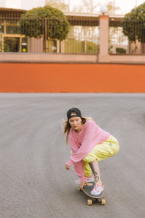 Free A young woman wearing colorful casual clothes skateboarding outdoors on a smooth road. Stock Photo