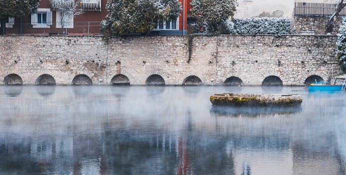 石墙上开着一道拱门，旁边坐落着房屋和树木，共同营造出宁静的冬日景象