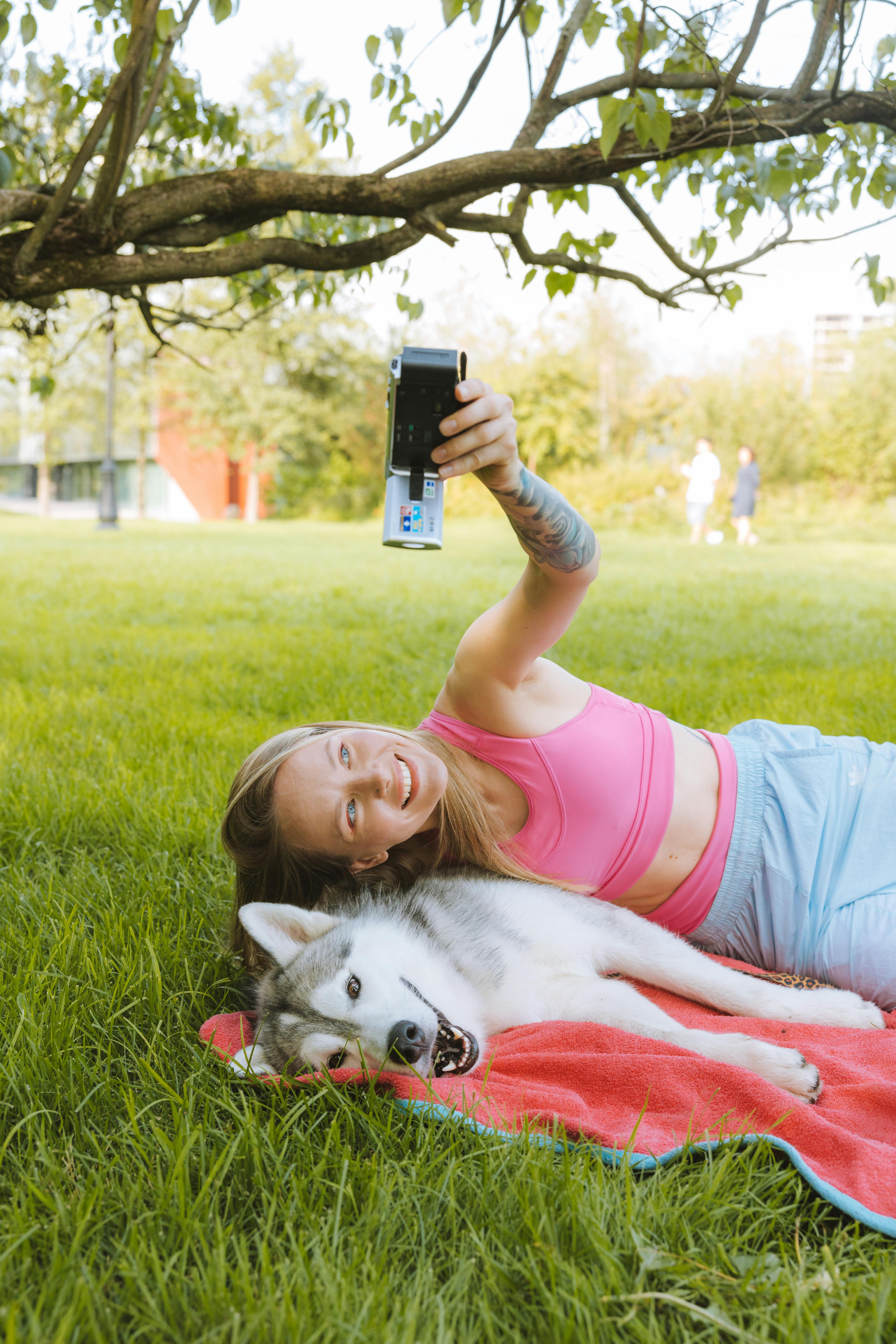 a woman in pink tank top lying beside a dog taking a selfie