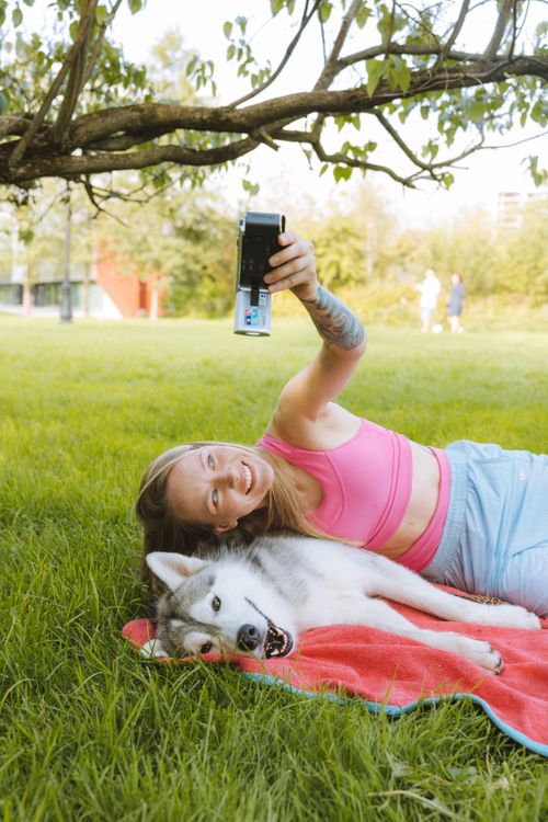 Free Smiling woman takes a selfie with her husky while lying on grass in a sunny park. Stock Photo