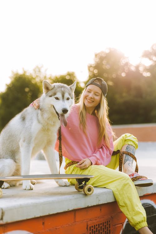 Free Smiling young woman with a husky on a skateboard at a skatepark during sunset. Stock Photo