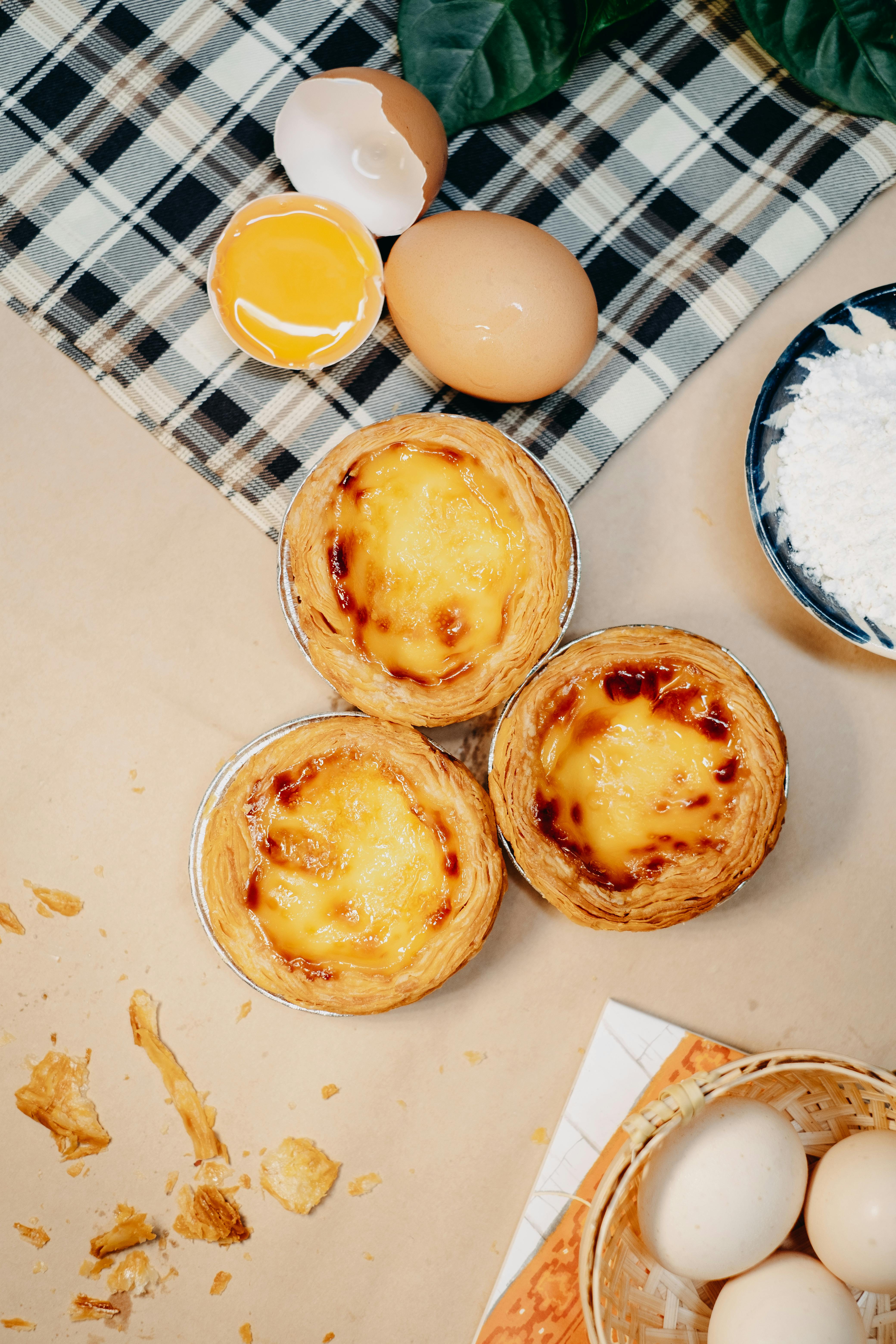 Overhead view of Portuguese custard tarts with ingredients on a rustic surface.