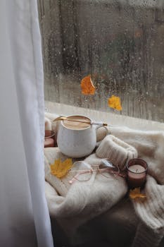 A warm, cozy autumn scene with coffee and candle by a rainy window.