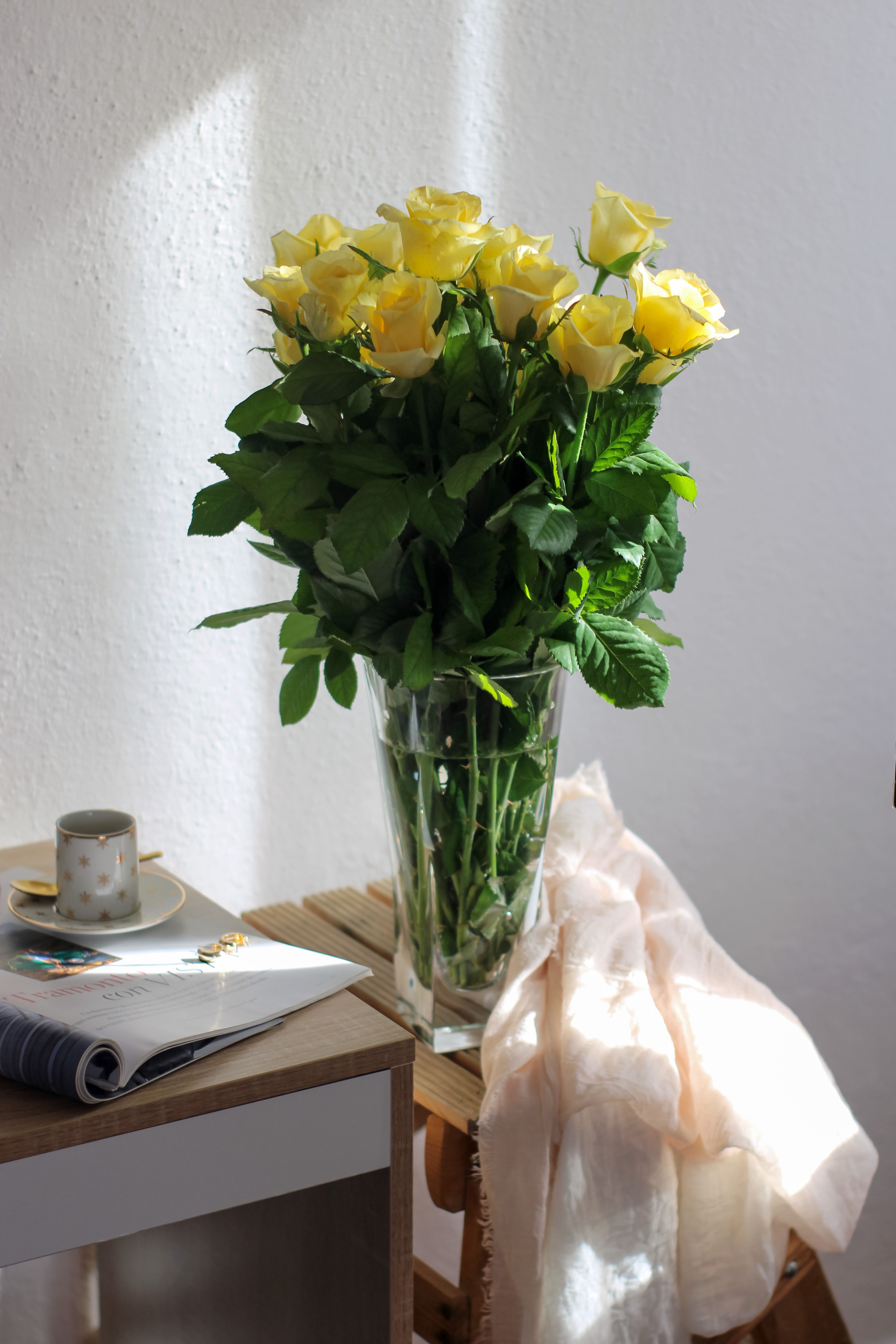 A beautiful arrangement of yellow roses in a glass vase next to a window. Captured in natural light.