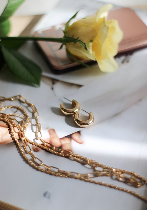 Jewellery and yellow rose laying on white surface