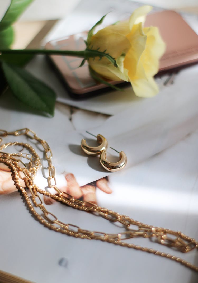 Jewellery And Yellow Rose Laying On White Surface