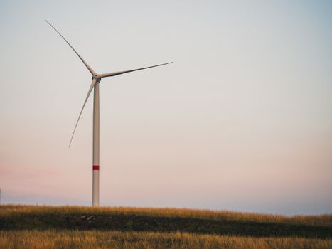 A solitary wind turbine stands on a hill under a colorful sunset sky, symbolizing sustainable energy.