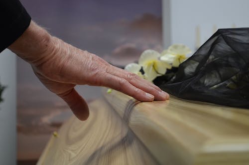 Free A touching moment of grief as a hand rests on a coffin, symbolizing loss and mourning. Stock Photo