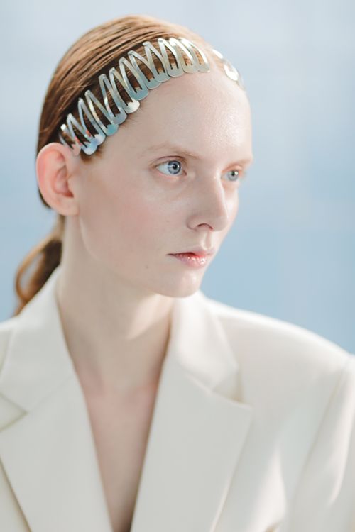 Free A stylish woman in a white blazer with a metallic hair accessory against a soft blue background. Stock Photo