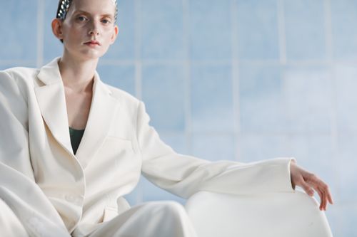 Free Stylish portrait of a woman in a white suit set against a minimalist blue background. Stock Photo