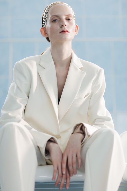 Free A sophisticated woman in a cream suit sits confidently against a light blue backdrop. Stock Photo