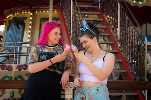 Two Women Standing Near a Carousel Holding Ice Cream in Cones