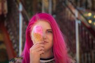 A woman with vibrant pink hair holding an ice cream cone with melted pink ice cream.