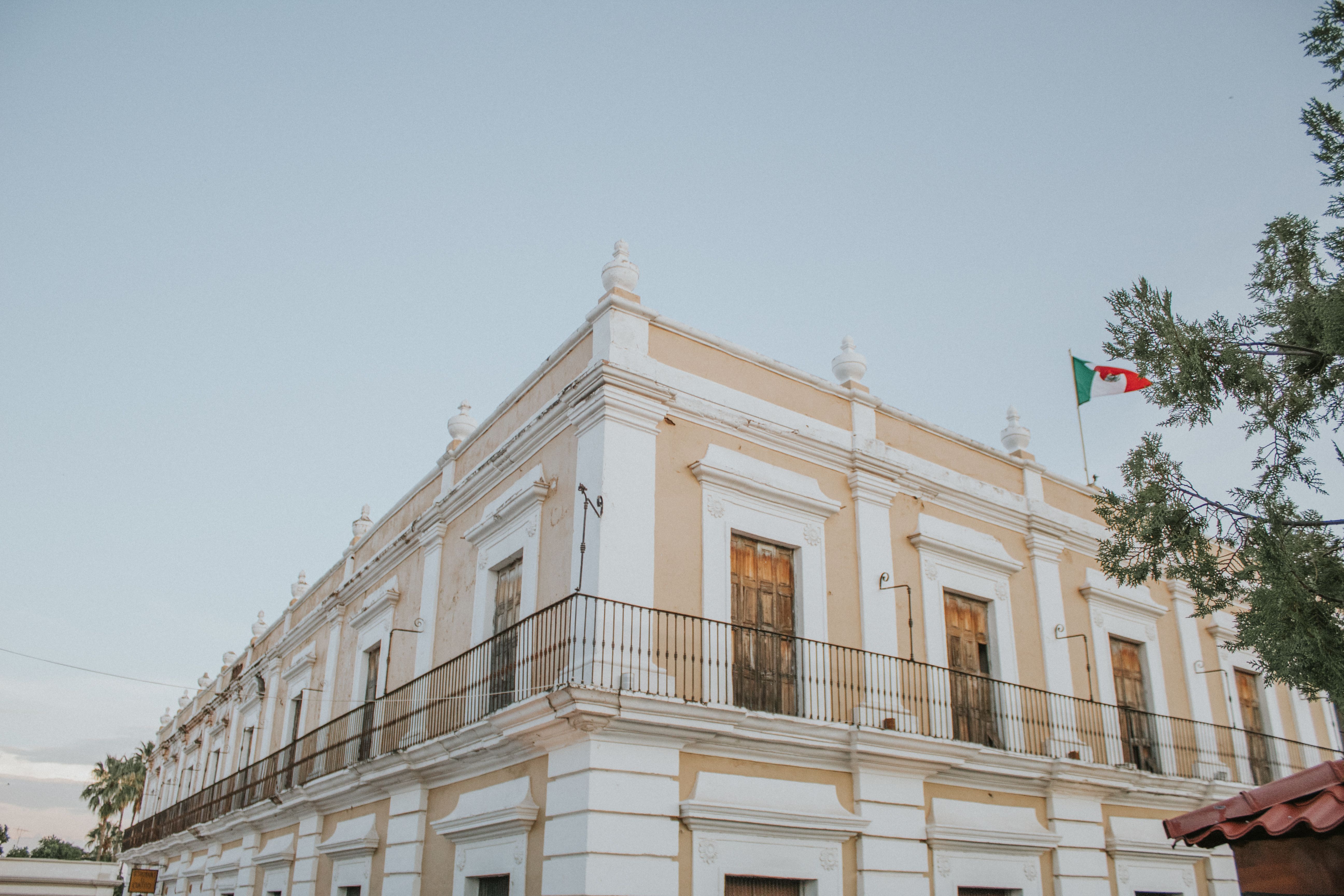 Elegant historic colonial building adorned with a Mexican flag under clear skies.