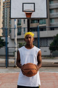 A young man stands holding a basketball on an outdoor court, conveying focus and determination.