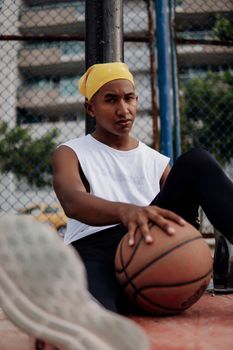 A young man in casual attire sitting on a court with a basketball, conveying relaxation and focus.