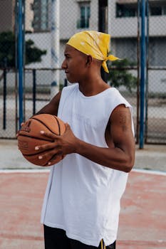 Profile of a young athlete holding a basketball on an outdoor court, wearing a yellow bandana.