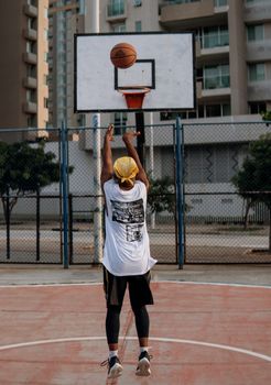 Rear view of a man shooting a basketball on an outdoor court during the day.