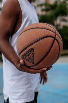 A man in a tank top holding a basketball on an outdoor court, showing athletic style.