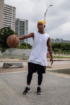 Young man holding a basketball in an urban setting with skyscrapers and overcast sky.