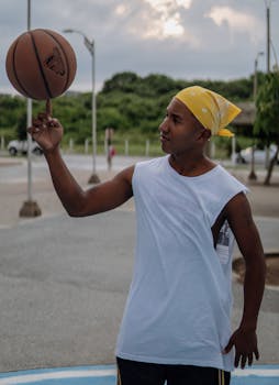 A young man skillfully spins a basketball on his finger outdoors, showcasing talent and balance.