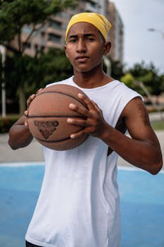 Confident young man holding a basketball on an outdoor court, ready to play.