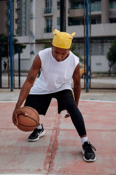 Athletic man in a tank top dribbling on an outdoor basketball court.