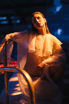 Artistic photo of a model by a pool in a white translucent robe at night.