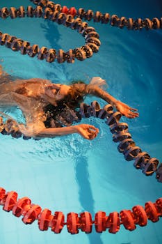 Woman swimming between lane ropes in a pool shot from above, highlighting elegance and motion.