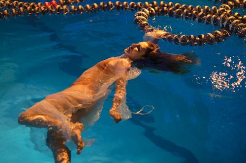 Free A serene portrait of a woman floating gracefully in a dimly lit swimming pool. Stock Photo