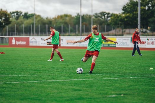 A young soccer player in a green bib practices kicking on a grassy field.
