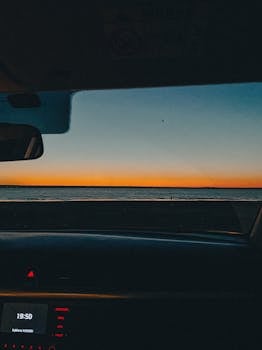 Experience a beautiful sunset through a car windshield with the ocean in view.