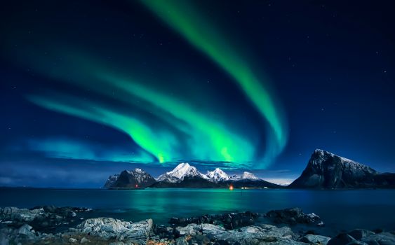 Breathtaking view of northern lights glowing over snowy mountains and calm waters at night.
