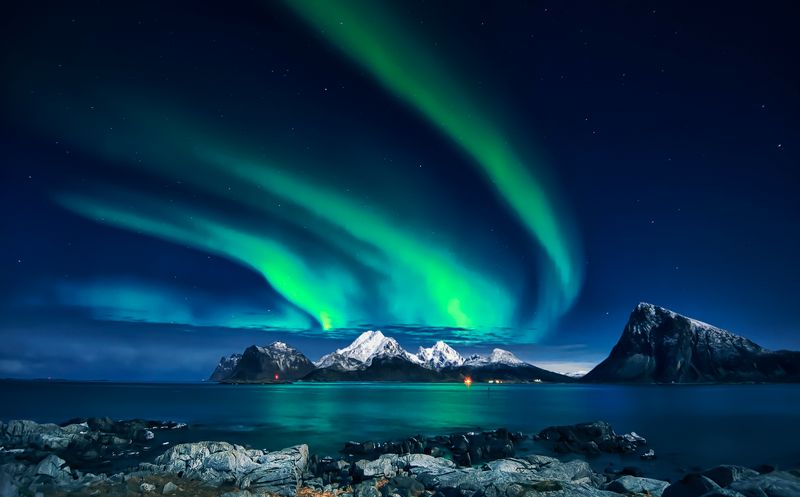 Aurora boreală magnifică deasupra munților și apei calme