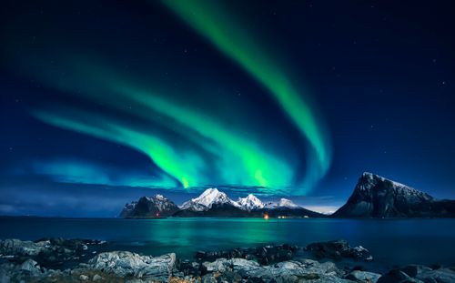 Free Breathtaking view of northern lights glowing over snowy mountains and calm waters at night. Stock Photo