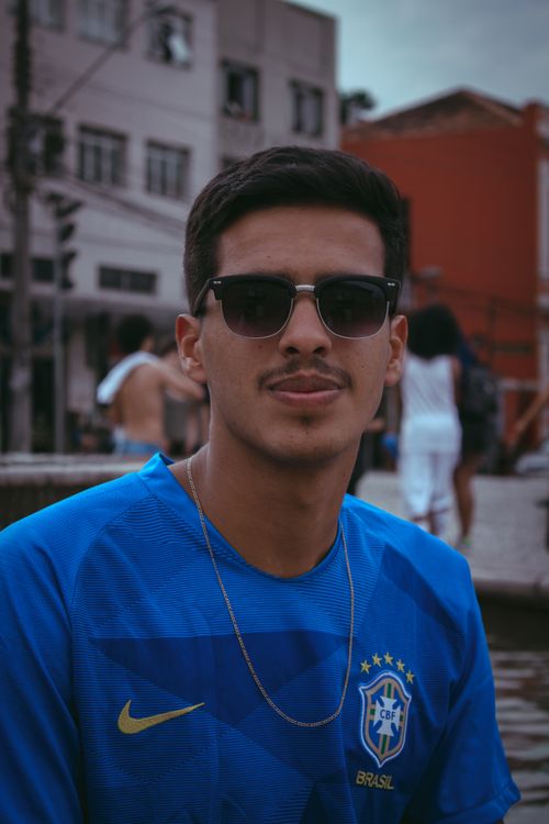 Free Portrait of a smiling young man in a blue sports jersey with sunglasses outdoors. Stock Photo