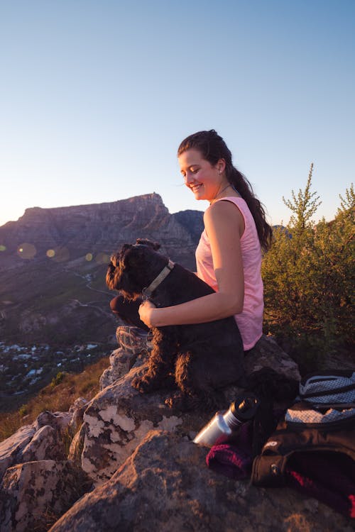 女人穿著粉紅色背心坐在狗旁邊的岩石上
