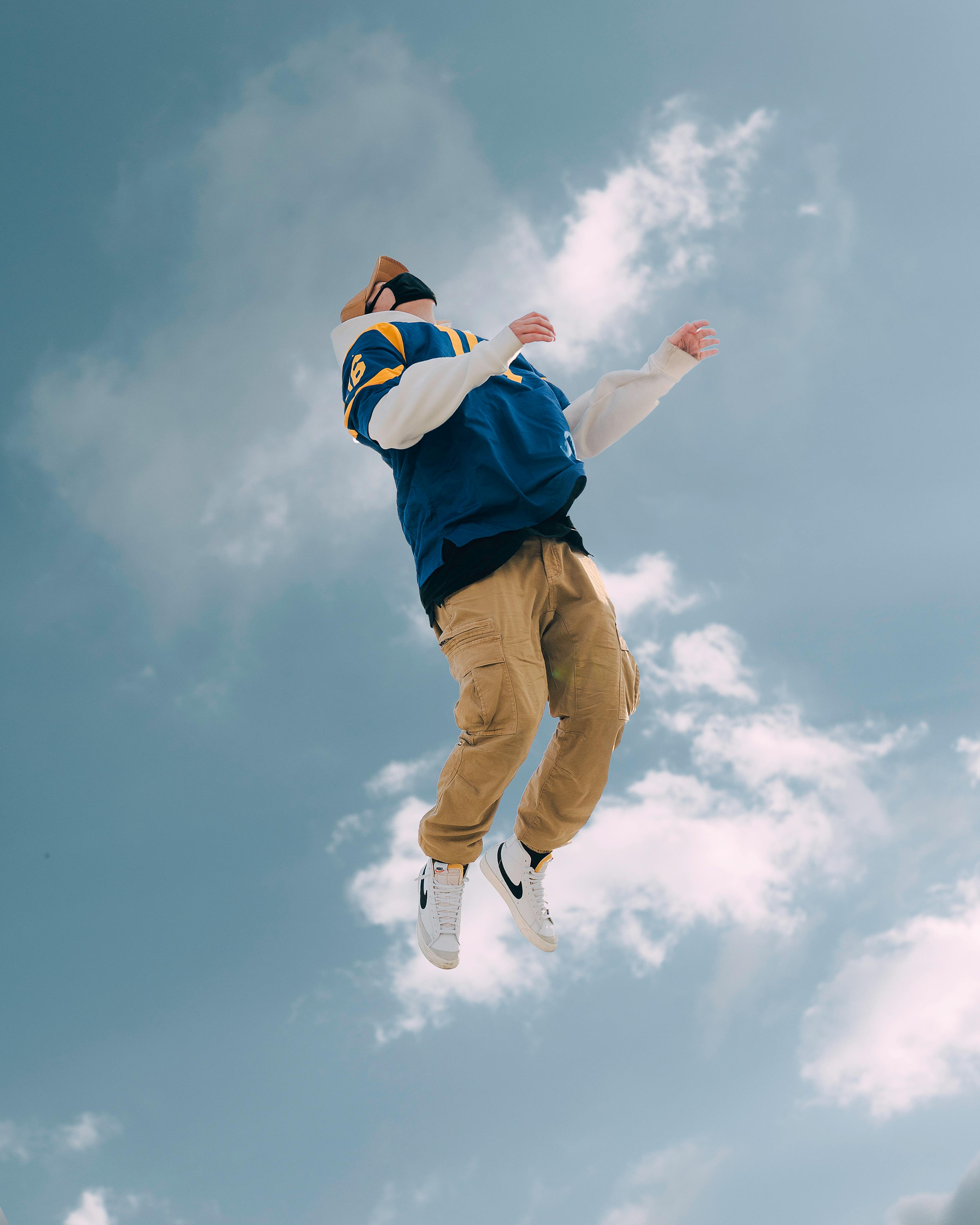 A stylish young man captured mid-jump against a vibrant blue sky, showcasing dynamic motion.