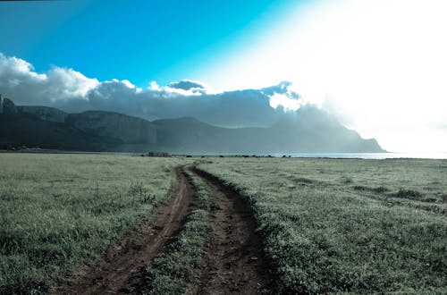 Green Grass Field Beside Brown Mountains Under White Cloudy Sky