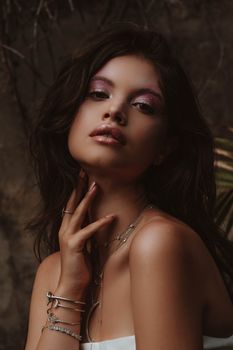 Graceful woman with makeup and jewelry, posing indoors with a serene expression.