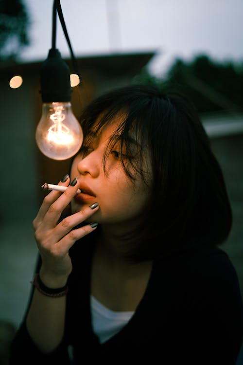 Free Close-Up Shot of a Woman Smoking near a Light Bulb Stock Photo
