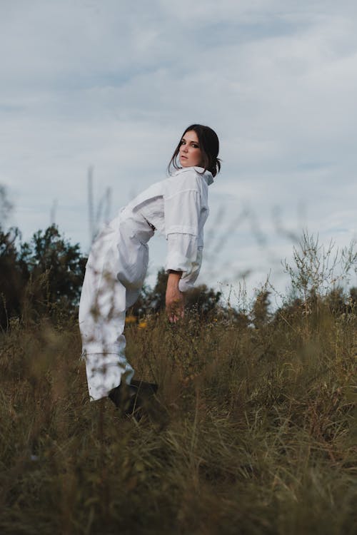 Woman in White Long Sleeve Shirt Standing on Brown Grass Field