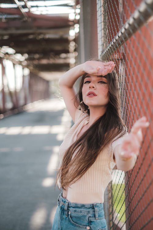 Woman in Beige Shirt Leaning on Chain Linked Fence