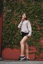 A Woman in Beige Sweatshirt and Black Short Standing Beside a Wall