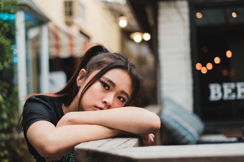 Free Portrait of a young woman resting her head on her arms at an urban outdoor cafe. Stock Photo