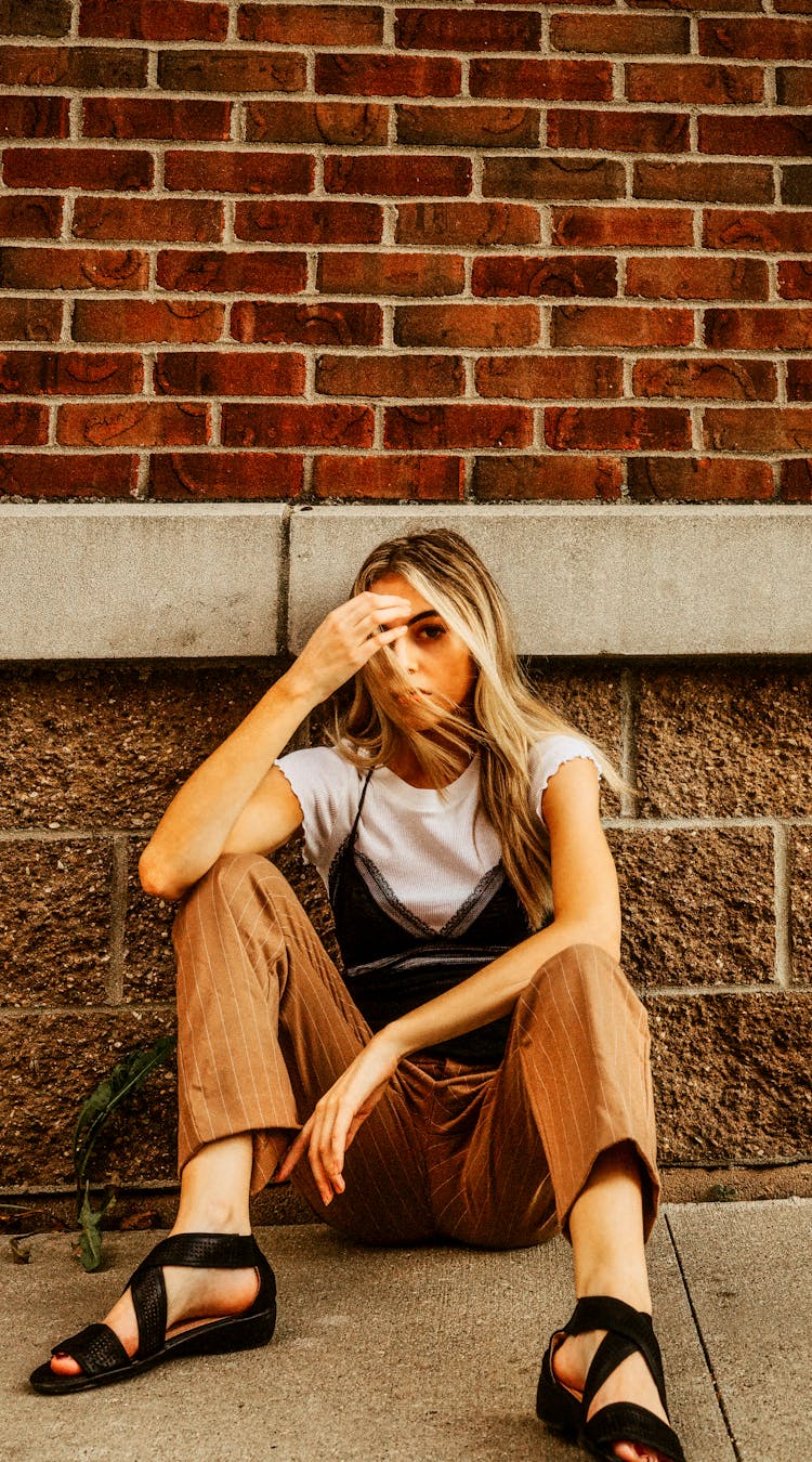 Girl Sitting On Ground On Street Near Building 