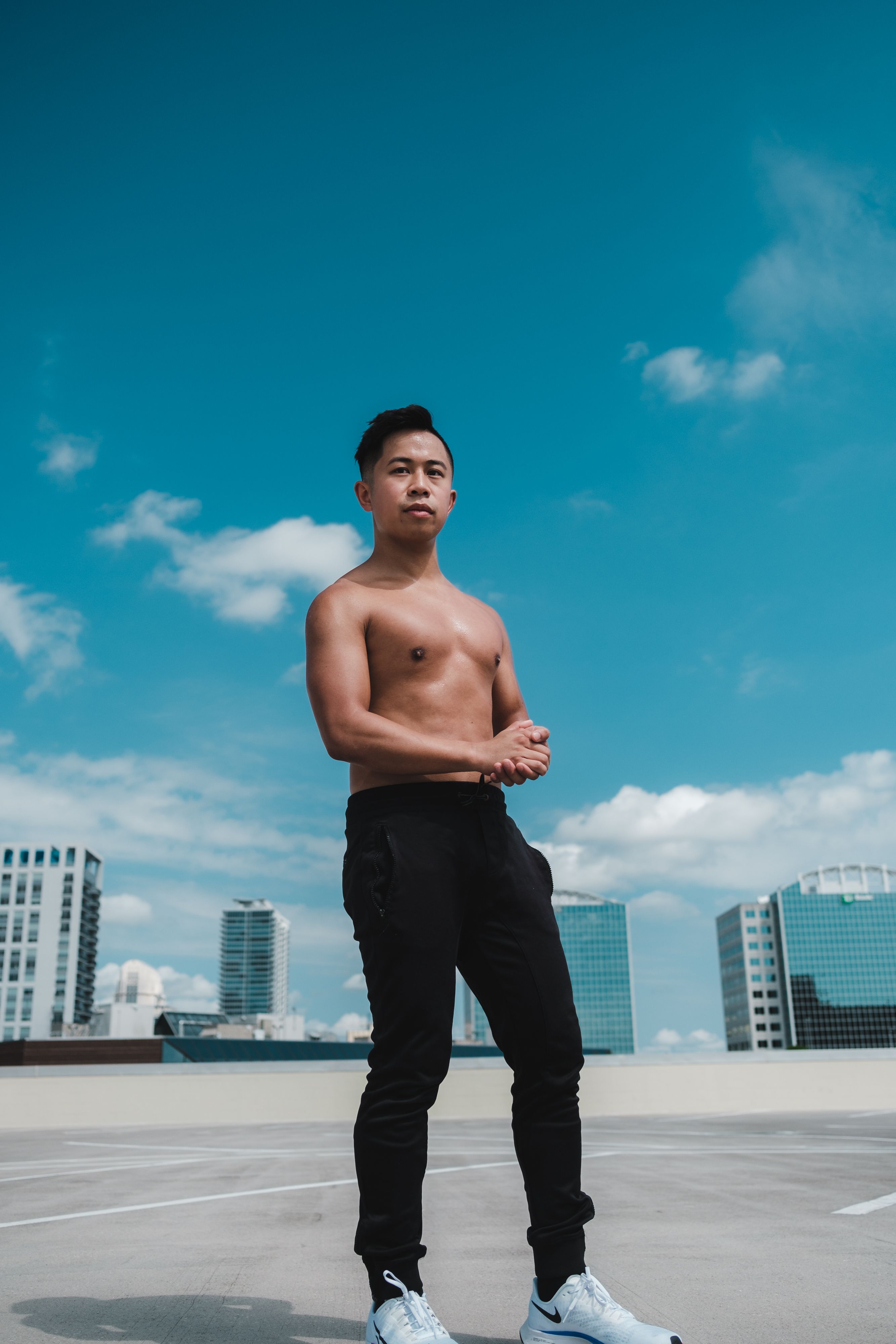 Shirtless Asian man in black pants stands confidently on a sunny rooftop in Orlando, Florida.