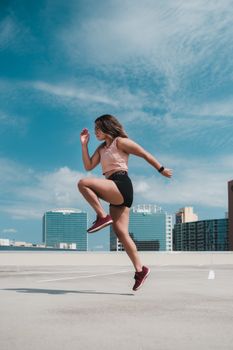 A woman doing a workout on a rooftop with a city skyline.