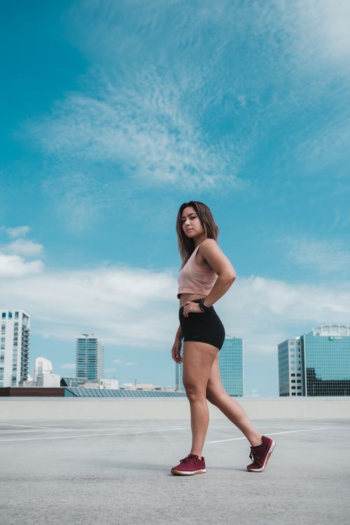 Free Stylish young woman in crop top and shorts posing on rooftop with city skyline in background. Stock Photo
