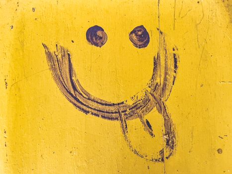 Close-up of a funny hand-drawn smiley face on a yellow wall with texture.